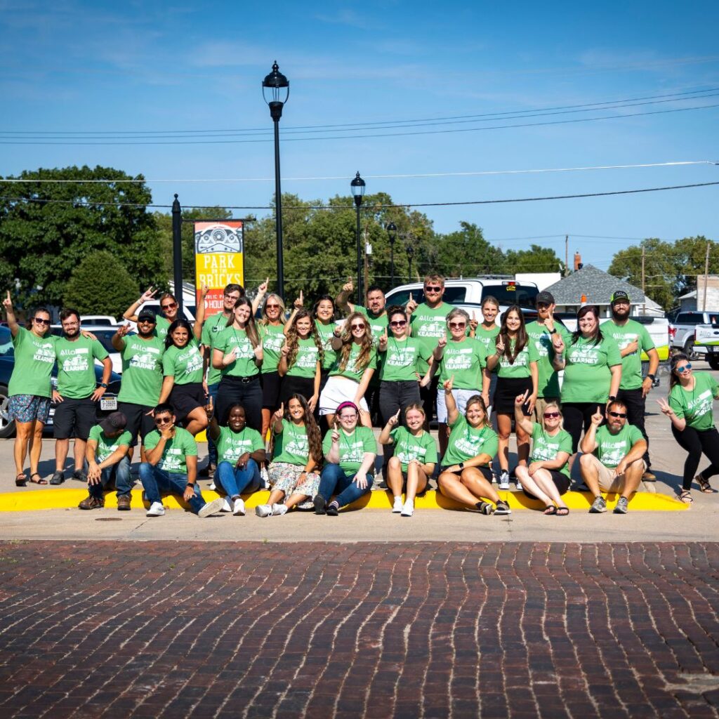 Image shows a group of ALLO employees sitting outside and pointing an index finger